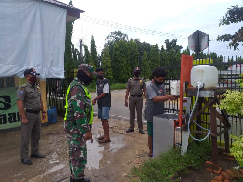 Walaupun Diguyur Hujan, Sertu Abdon Pordusi Tetap Ingatkan Warga Agar Pakai Masker Saat Beraktivitas